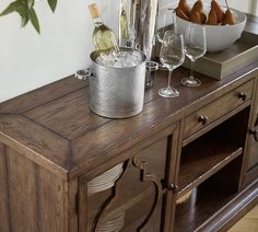 a wooden table with wine glasses and bottles on it next to a bowl of fruit