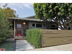 a house that has a red door and some bushes in front of it with trees