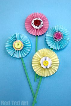 three colorful paper flowers on a blue background with a button in the center and two green stems