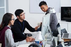 three people sitting at a desk working on a computer and holding a coffee cup in front of them