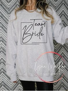 a woman wearing a sweatshirt that says team bride on the front, and black lettering on the back