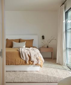 a large bed sitting next to a window in a room with white curtains and pillows