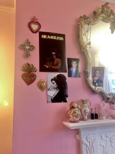 a pink wall with pictures and other items on the mantle in front of a mirror