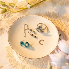 three pairs of earrings are sitting on a white plate next to some flowers and lace