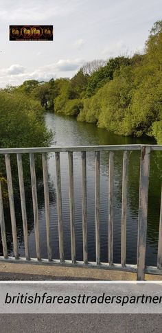 there is a bridge over the water with trees in the back ground and an overhead sign above it that says british fasttraderspartners