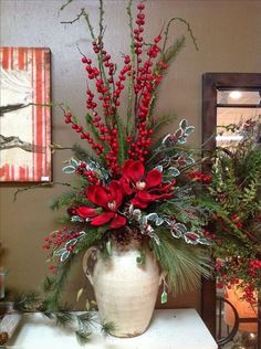 a white vase filled with red flowers and greenery on top of a table next to a mirror