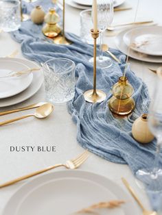 the table is set with white plates and gold utensils, silverware, and blue napkins