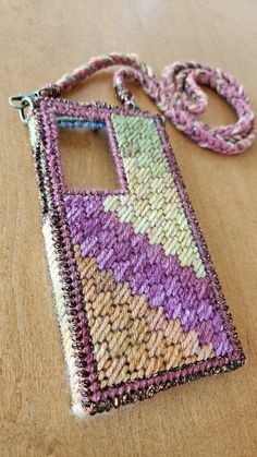 a cell phone case made out of knitted material on a wooden table with a lanyard