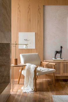 a white chair sitting in front of a wooden wall next to a table with a lamp on it