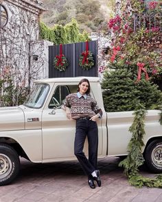 a woman leaning on the back of a white truck with christmas trees in the bed