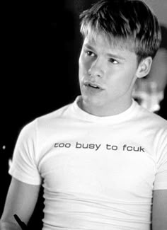 black and white photograph of a young man wearing a t - shirt that says, coo busy to four