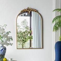 a blue chair sitting next to a table with a vase on it and a mirror above it