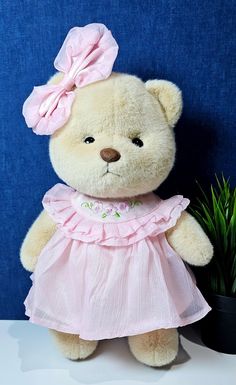 a teddy bear wearing a pink dress next to a potted plant