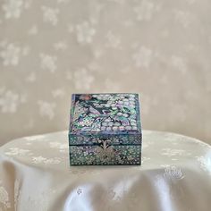 a decorative box sitting on top of a white tablecloth covered table with floral designs