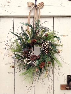 a wreath with pine cones and evergreens hanging on a white wooden door decorated for christmas