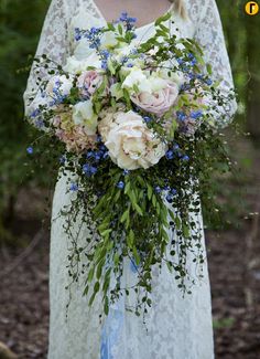 a woman holding a bouquet of flowers in her hands and wearing a white lace dress