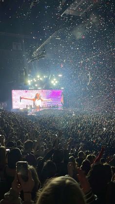 a large crowd at a concert with confetti falling from the ceiling and on to the stage