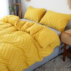 a bed with yellow comforters and pillows in a room next to a table, wicker basket on the wall