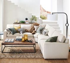 a living room with white couches and pillows on top of the sofa, next to a coffee table