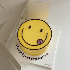 a yellow smiley face cake sitting on top of a white table next to a box