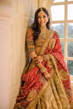 a woman in a red and gold bridal gown posing for the camera with her hands on her hips