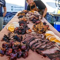 a man standing next to a table full of meats and other foods on it