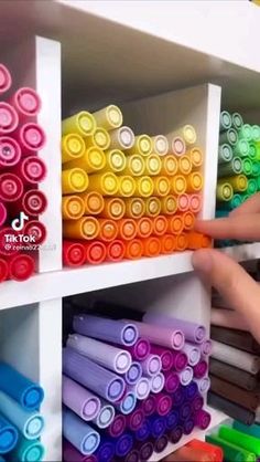 the shelves are filled with many different colored crayons and there is a hand reaching for one