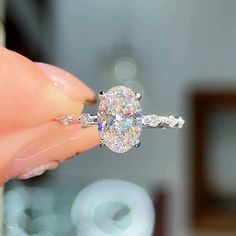 a close up of a person holding a ring with an oval shaped diamond on it