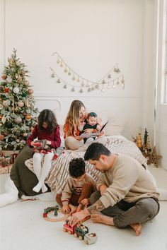 a group of people playing with toys on the floor in front of a christmas tree