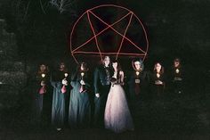 a group of people standing next to each other in front of a red pentagram