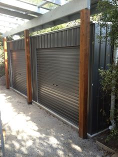 an outdoor area with a large metal garage door and wooden posts, surrounded by greenery