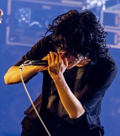 a man with long black hair holding a microphone to his ear while standing on stage