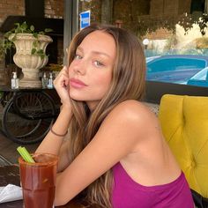 a beautiful young woman sitting at a table with a drink in front of her face