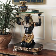 an egyptian statue is holding a tray on it's shoulder and potted plant in the background