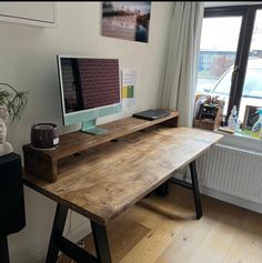 a wooden desk with a computer on it in front of a window and a potted plant