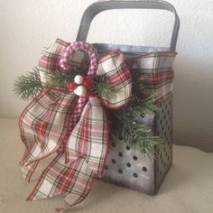 a metal basket with a christmas bow on the handle and pine branches hanging from it