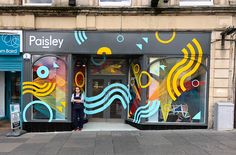 a woman standing in front of a store with colorful paintings on the windows and doors