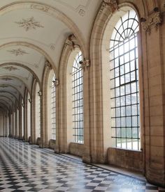 an ornate hallway with large windows and black and white checkered flooring on both sides