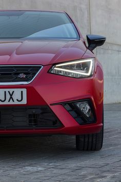 the front end of a red car on a cobblestone street with a concrete wall in the background