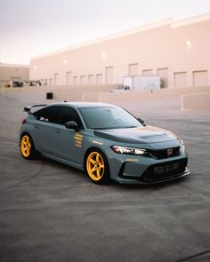 a gray car with yellow rims parked in front of a building on the street