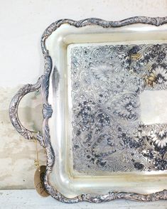 an ornate silver tray with flowers and leaves on the bottom is sitting against a wall