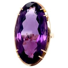 This large enchanting 14.50 carat faceted elongated oval amethyst is set in a mid-century modern 14 karat yellow gold setting that has a rose gold hue. This amethyst's rich deep purple comes alive in the light enhancing its brightness. The stone measures approximately 1 1/16" long by 1/2" wide and is held in the mounting by four stations of double prongs. Under the gem, the mounting appears as a frame highlighting the beauty of the stone in this circa 1970 mounting making the top of the ring approximately 1 1/4" long by 5/8" wide. This vibrant amethyst is very clean with no visible inclusions. The ring rises approximately 7/16" off the finger, is a US size 6.5, and weighs 9.1 grams. The 1970's was a decade of punk rock and disco, social change, and iconic movies such as The Godfather, Star Musica Disco, Yellow Gold Cocktail Ring, Green Sapphire Ring, Amethyst Gold, Gold Statement Ring, Gold Cocktail Ring, Gold Cocktail, Honey Colour, Diamond Ring Settings