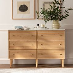 a wooden dresser sitting next to a wall with pictures on it and a potted plant