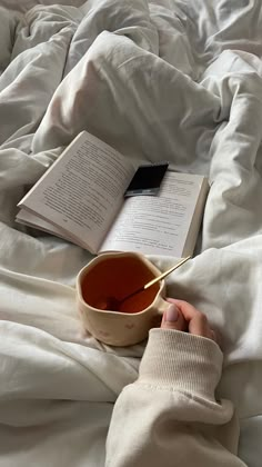 a person is reading a book and drinking tea in bed