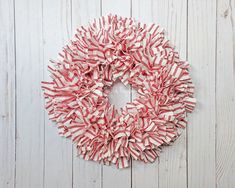 a red and white wreath hanging on the side of a wooden wall next to a pair of scissors