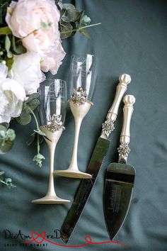 three wine glasses and a knife sitting on a bed next to some flowers with green satin