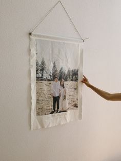 a woman holding up a photo hanging on the wall next to a man in a white shirt