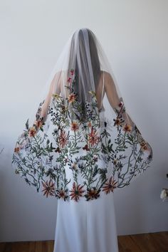 the back of a bride's veil with flowers and leaves on it, in front of a white wall