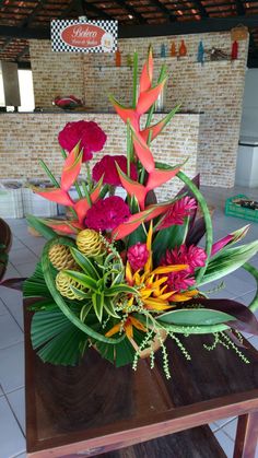 an arrangement of flowers on a table in a room with tile flooring and brick walls