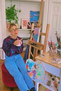 a woman sitting on a chair in front of a easel holding a paintbrush